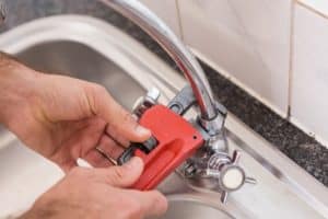 A plumber tightens a leaky faucet with a pipe wrench