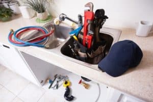 A plumber's tools and assorted hardware in a kitchen sink