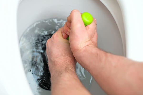 A man tries to unstop his toilet with a plunger